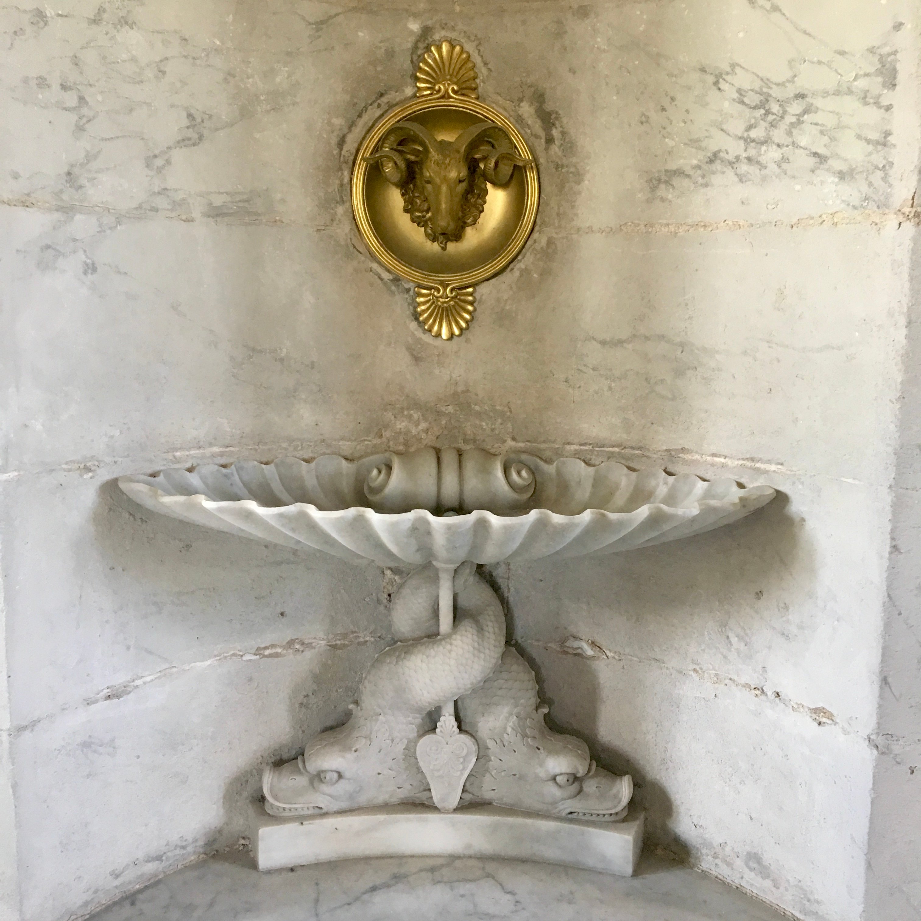 Gold and marble fittings from the interior of the Queen's Dairy in her Hamlet. A golden tap shaped like a ram's head sits above a marble sink held up by carved fishes.